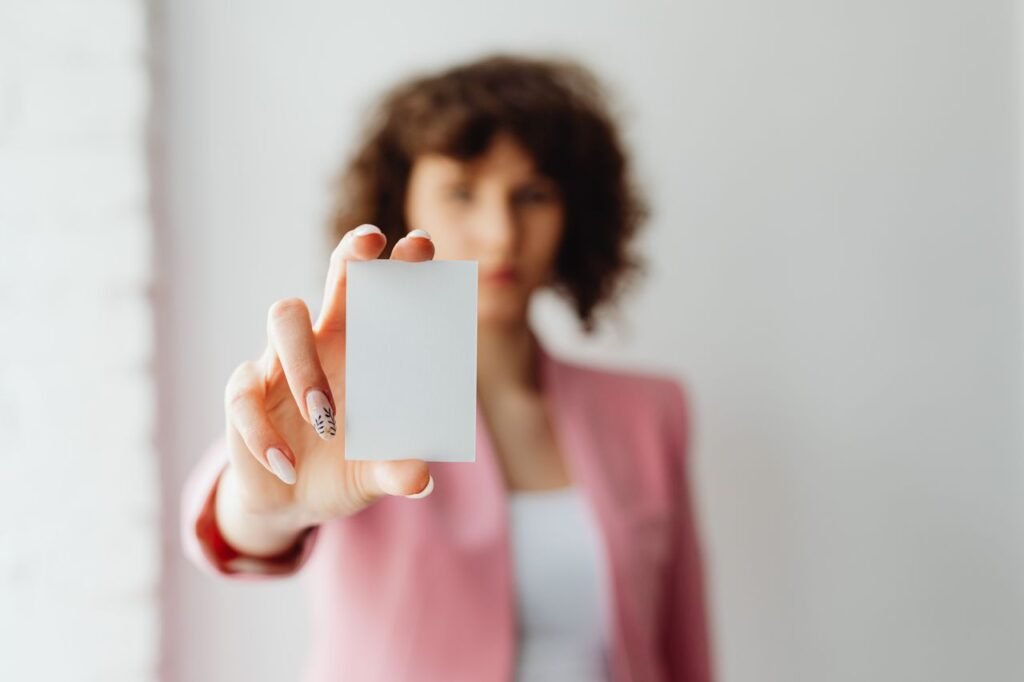 Crafting Captivating Headlines: Your awesome post title goes here A woman with curly hair in a pink jacket holds a blank card, focus on the card.